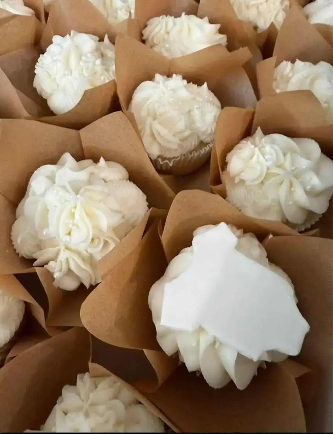 Freshly baked white cupcakes with frosting in brown paper cups.