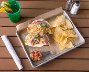 Street corn tacos with chips and a green drink on a wooden table.