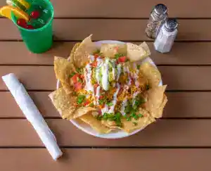 Plate of loaded nachos with cheese, salsa, sour cream, and green onions.
