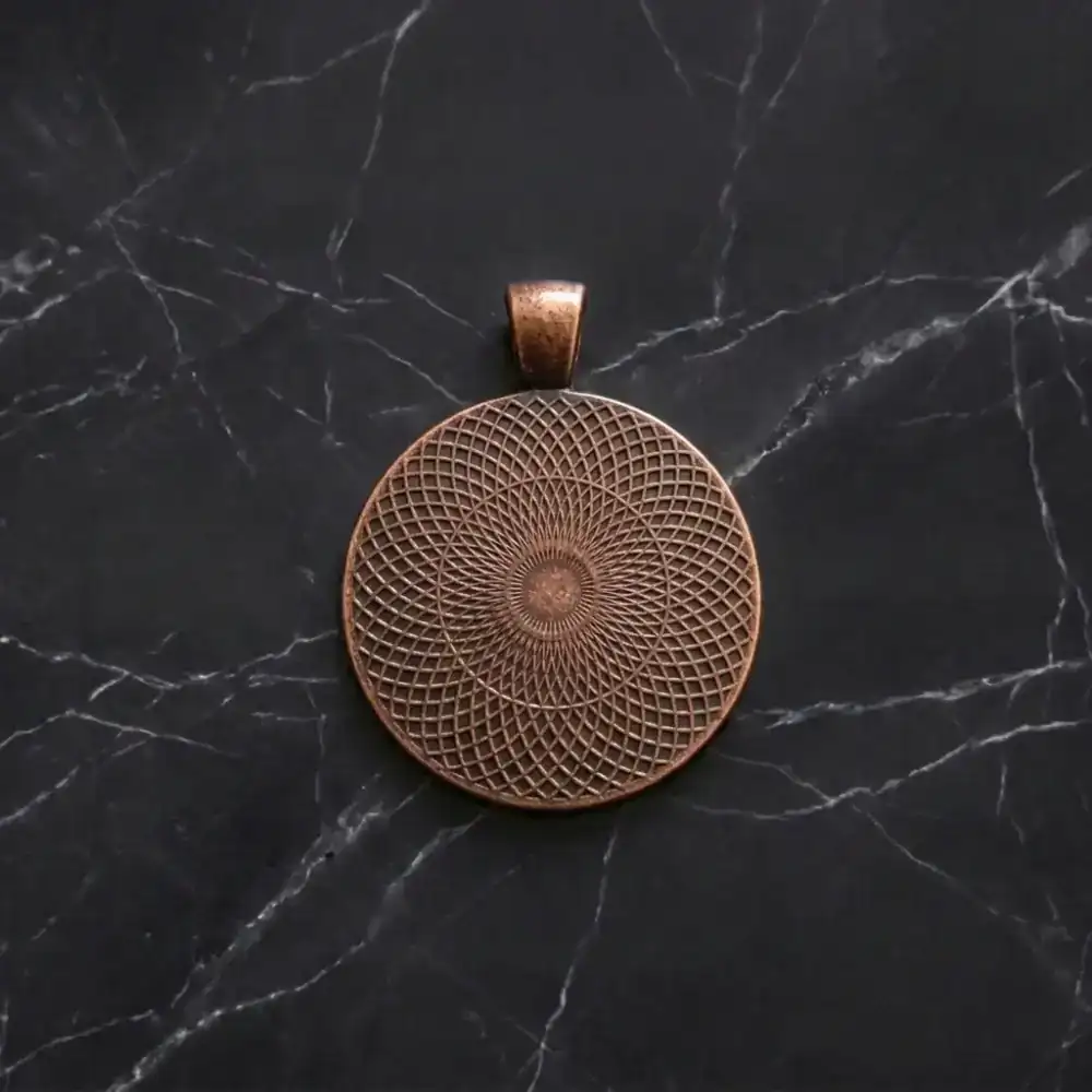 Textured lattice pattern on the back of an antique red-bronze round pendant setting lying on a dark marble surface.