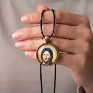 Person holding a round Jesus Christ Pantocrator glass cabochon necklace over their hand to show wearable scale.