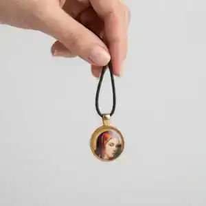 Hand holding the Theotokos in Grief religious pendant by its black cord against a clean studio background.