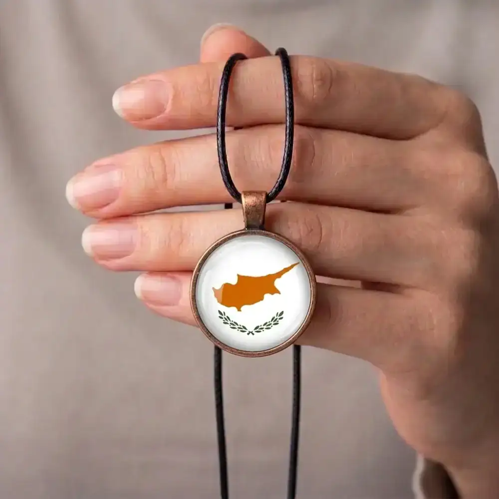 Cyprus Flag Pendant Hand Held Display Person holding a Cyprus flag glass cabochon pendant necklace with a black cord cord looped over their fingers.