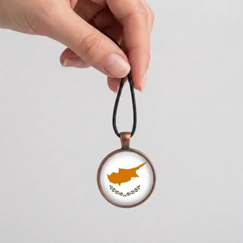 Cyprus Flag Pendant Hanging Hand Display Hand holding the top loop of a black cord displaying the suspended round Cyprus flag pendant.