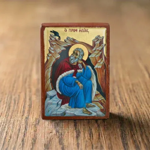 Prophet Elijah wooden mounted icon with the prophet seated in a rocky cave and a raven above, displayed on a wooden table