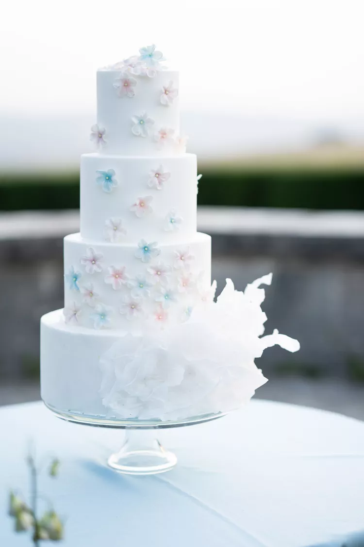 Elegant four-tier white wedding cake with delicate pastel sugar flowers, perfect for luxury destination weddings in Tuscany.