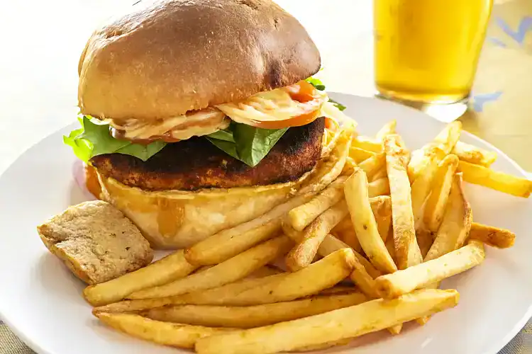 Delicious blackened chicken sandwich with lettuce, tomato, and sauce on a bun, served with fries and.