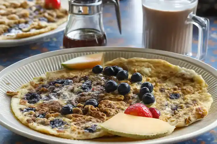 Fresh blueberry pancake with strawberries and cheese on a white plate.