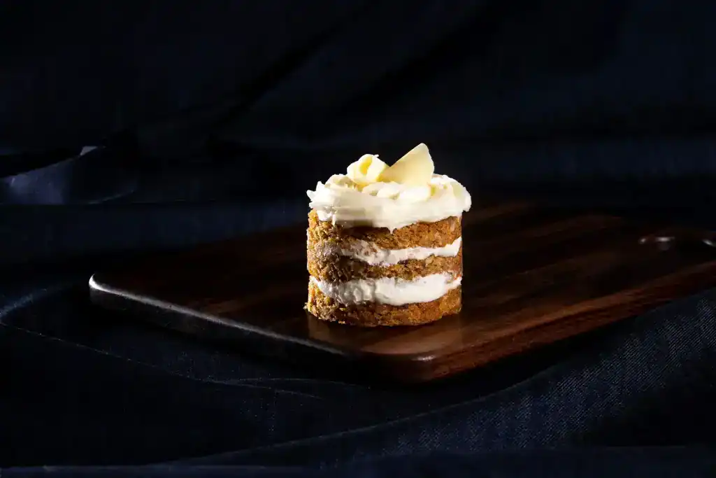 Delicious carrot cake slice with cream cheese frosting and white chocolate shavings.