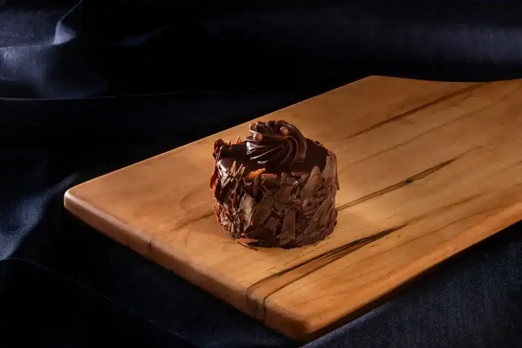 Chocolate mousse cake slice on wooden board with chocolate shavings.