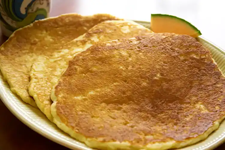 Stack of golden-brown buttermilk pancakes on a plate with a slice of melon.