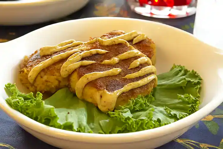 Crab cakes served on lettuce with mustard sauce drizzle.