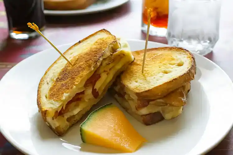 Delicious egg and cheddar cheese sandwich on toasted bread with melon slice.