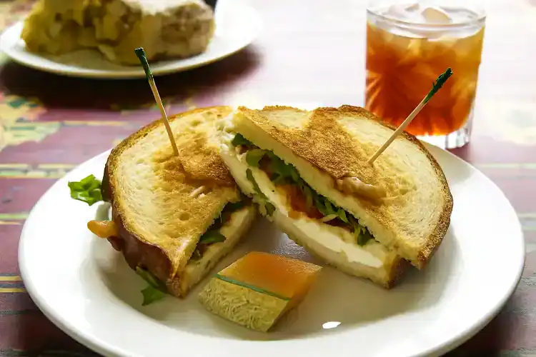 Close-up of a hearty breakfast sandwich with eggs, cheese, and greens on toasted bread.