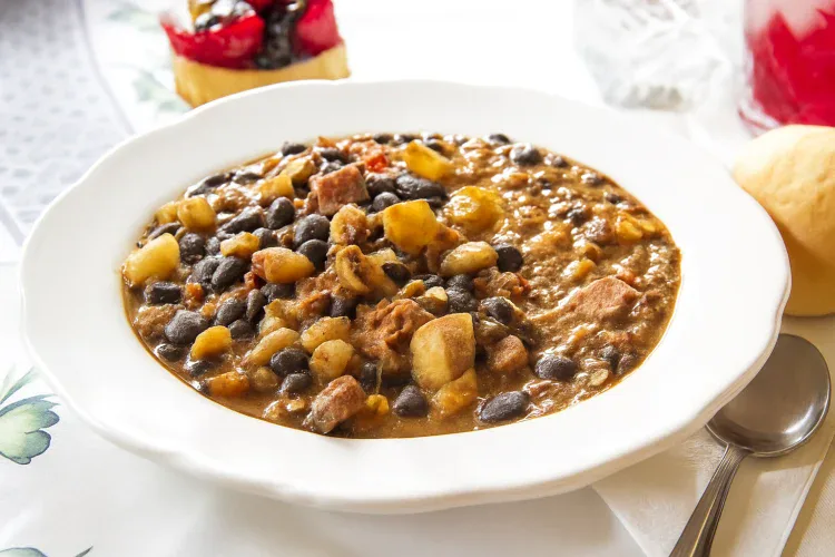 Traditional Brazilian feijoada with black beans and pork in a white bowl.