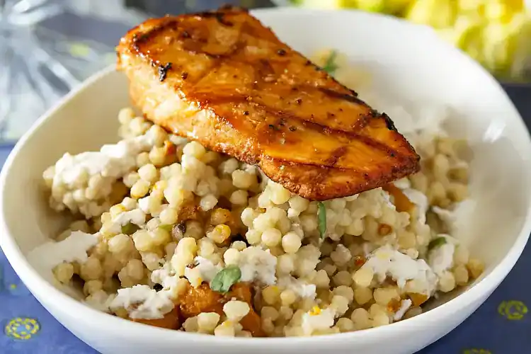 Salmon fillet on a bed of Israeli grain bowl with vegetables.