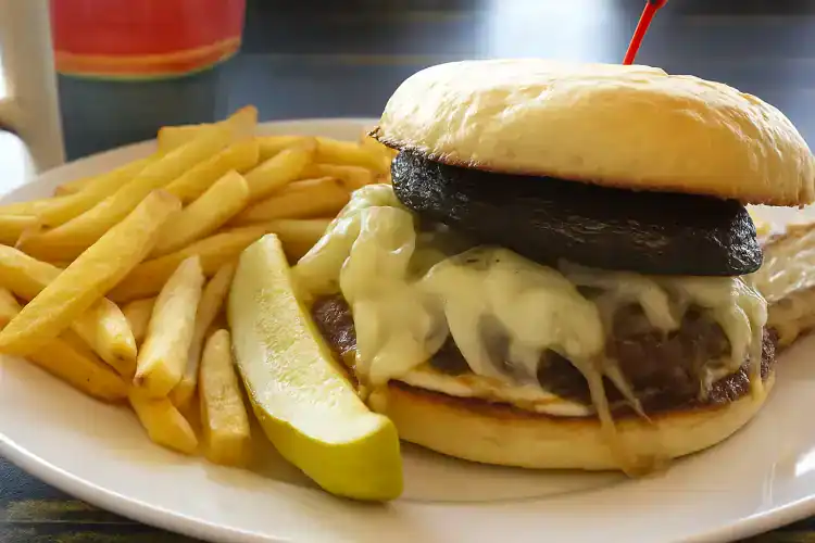 Delicious mushroom burger with fries and lemon wedge on a plate.