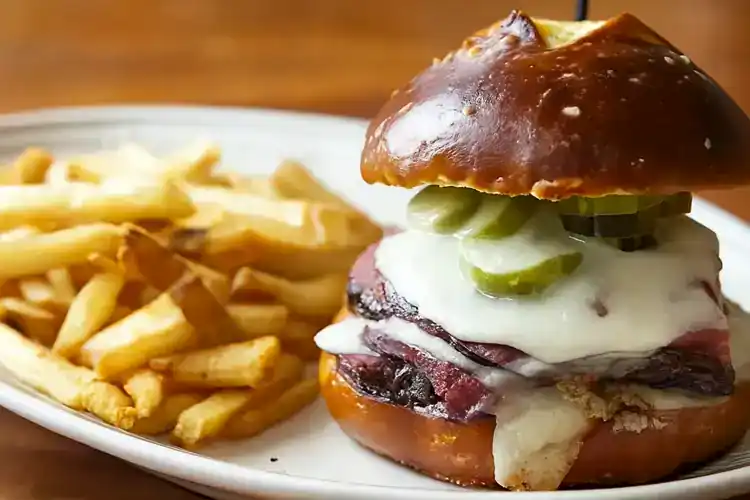 Delicious Pastrami Pretzel Sandwich with cheese and pickles on a bun.