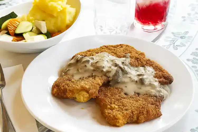 Crispy pork schnitzel with creamy mushroom sauce on white plate.