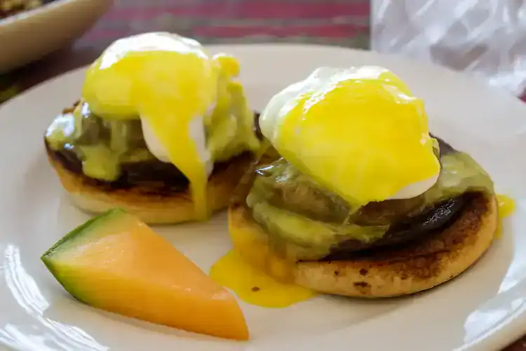 Steak Benedict with poached eggs, avocado, and hollandaise sauce on an English muffin.
