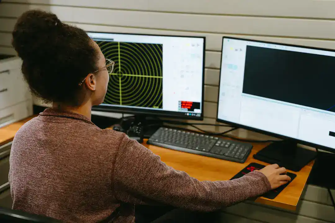 Woman working on dual monitors with radar and data analysis software.