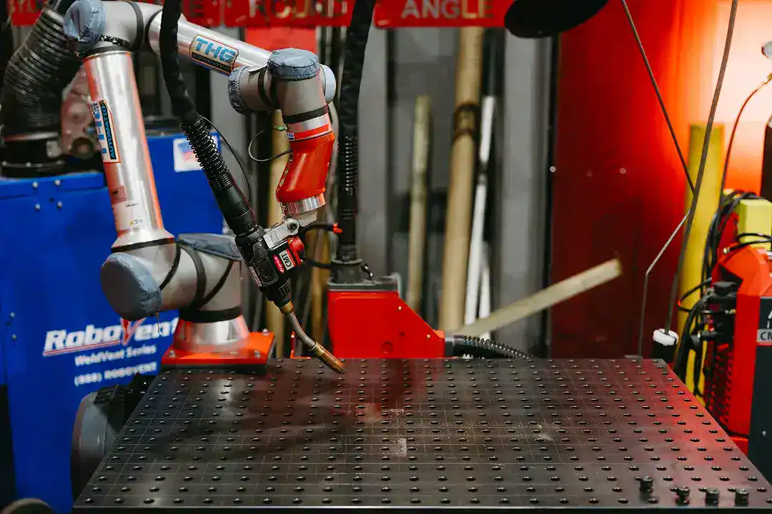 Industrial robotic arm welding metal on a perforated worktable at Active Manufacturing.