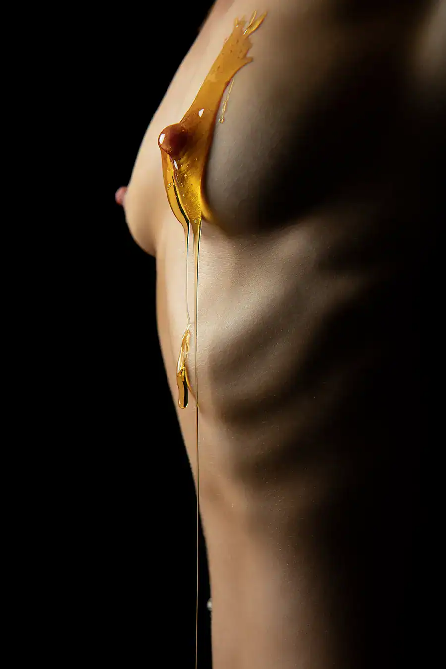 Close-up of a woman's body with honey dripping down her breast, creating an artistic and sensual image. The dark background emphasizes the glossy texture and sensual form, highlighting the fluidity and contrast