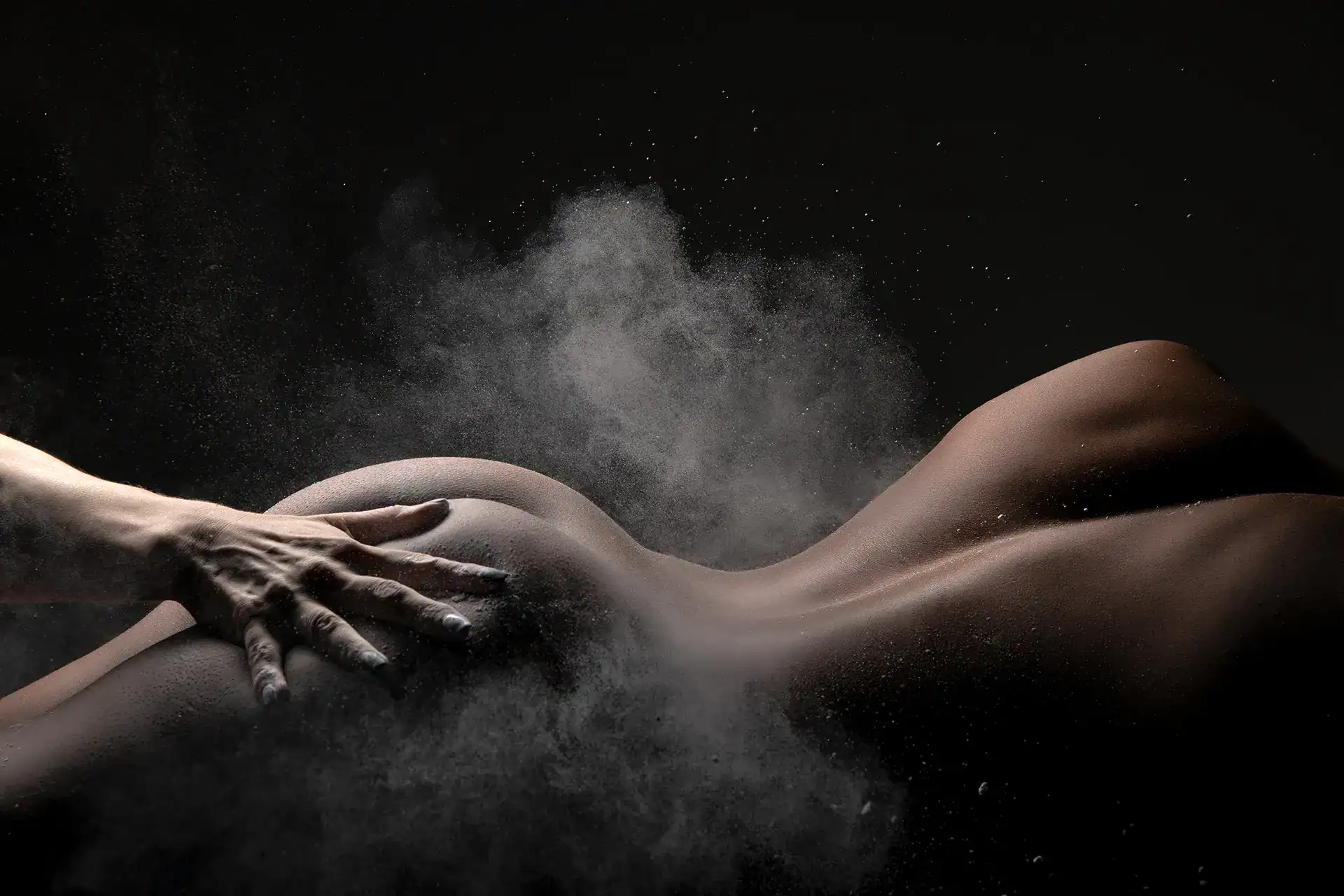 Dramatic fine art nude of a woman’s back and buttocks as powder explodes on impact from a hand, captured in a conceptual nude photography shoot by a creative studio artist in South Africa
