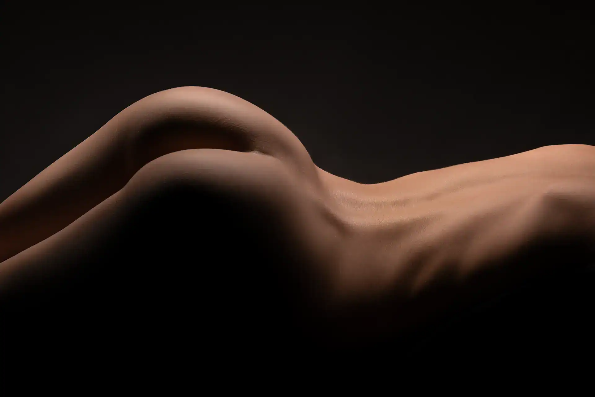Abstract nude photograph of a woman lying on her side, curves and spine softly illuminated against a dark backdrop, celebrating the elegance of the female form in Johannesburg bodyscape photography