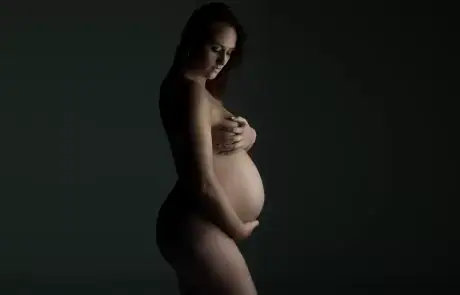 Erotic nude photo of a woman holding half a grapefruit against her pubic area, middle fingers pressed into it suggestively with juice dripping, evoking a bold, phallic visual metaphor