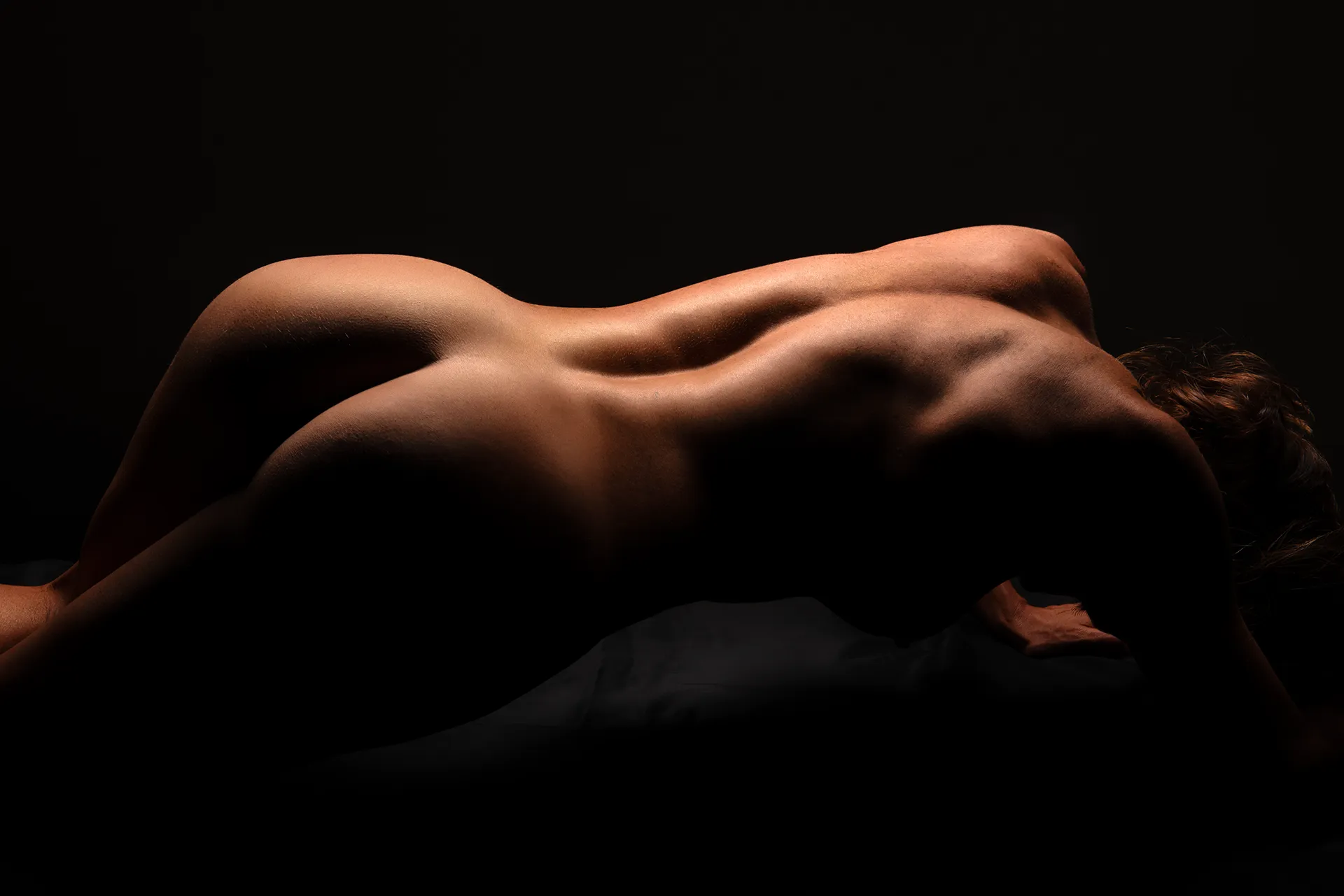 Artistic nude bodyscape featuring the elegant curves of the human form, captured in shadow and light to emphasise texture, contour, and the beauty of natural silhouette