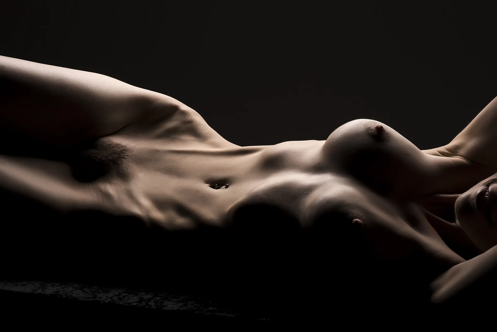 Artistic nude photograph of a woman posed with dramatic lighting and shadow, highlighting the curves and contours of her body as a visual form of expression