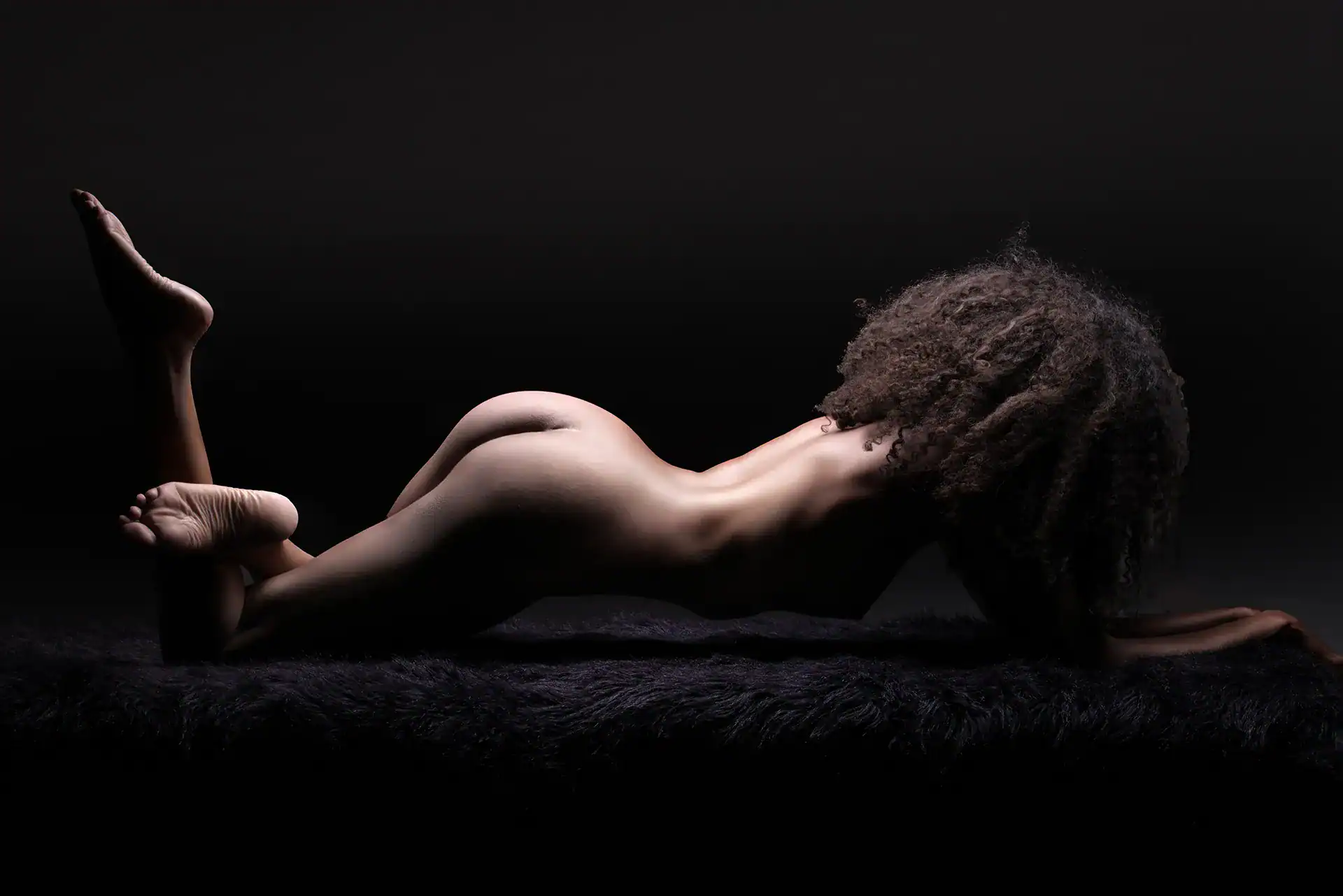 Full-body nude of a Black woman with afro hairstyle lying on faux fur, bum arched and curves celebrated