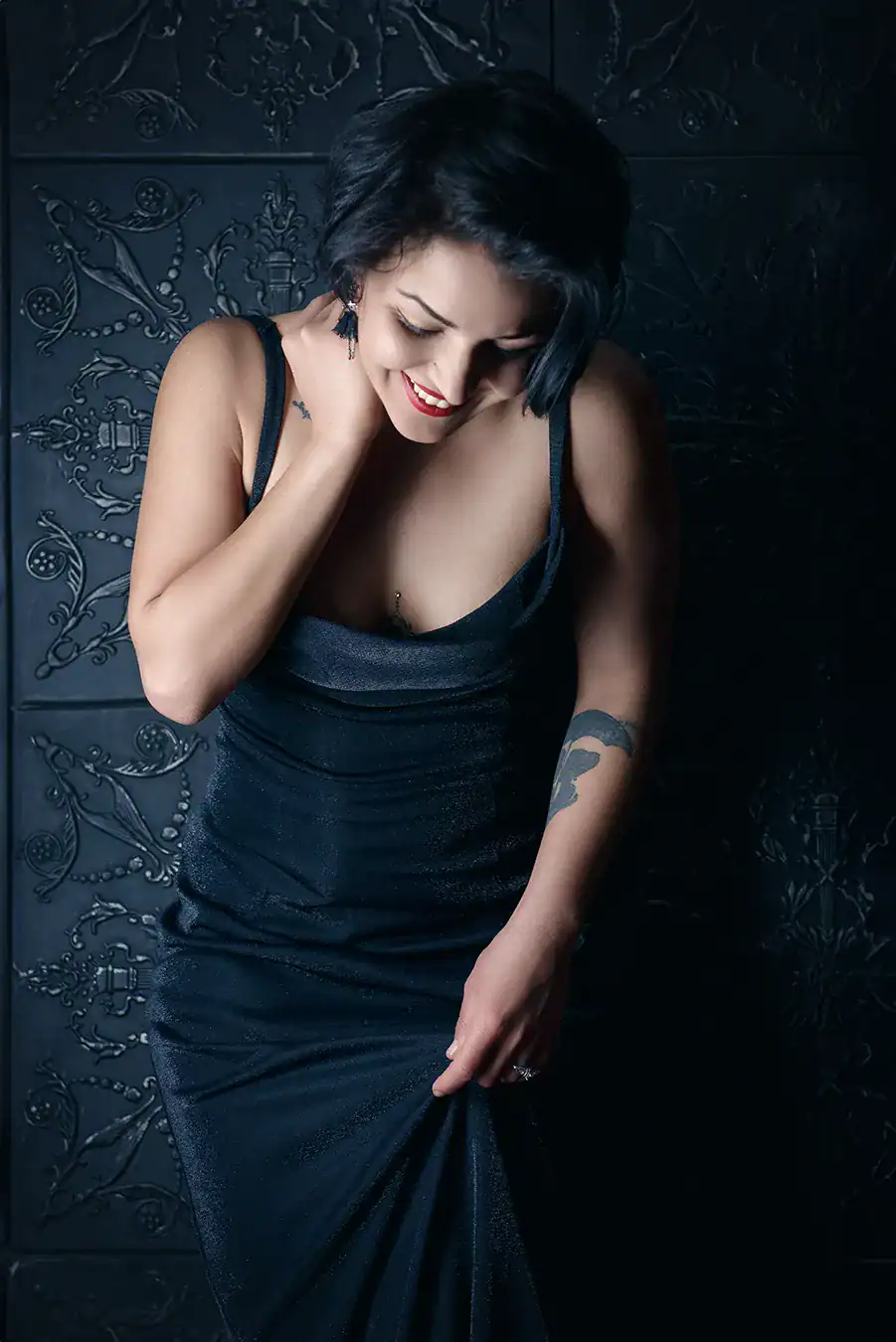 Boudoir portrait of smiling woman in shimmering black gown with dark backdrop, exuding elegance and quiet confidence