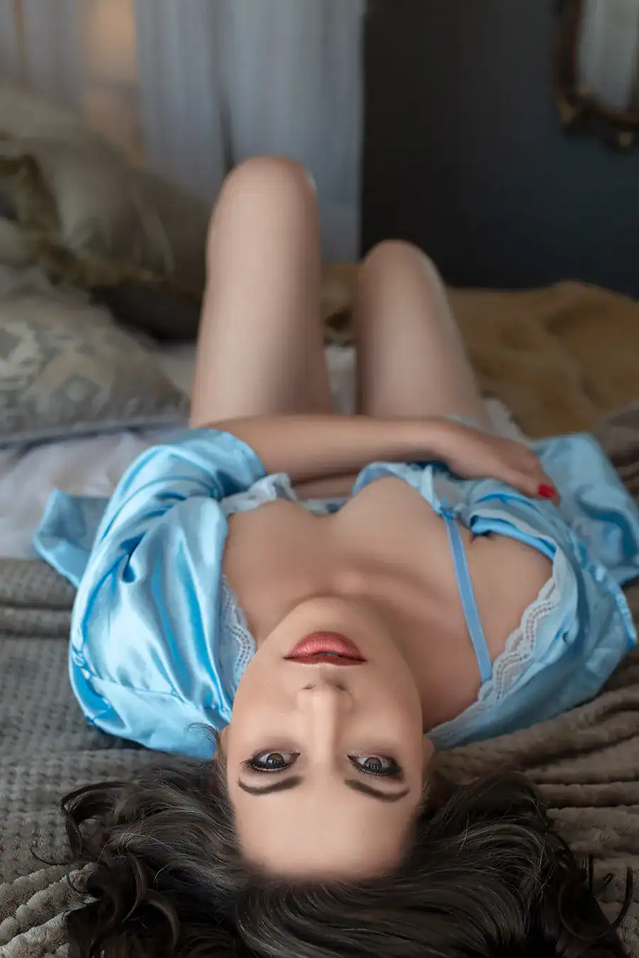 Woman in powder blue satin robe and lace bra lying on bed with soft bedding, gazing upward in a gentle boudoir moment, Johannesburg