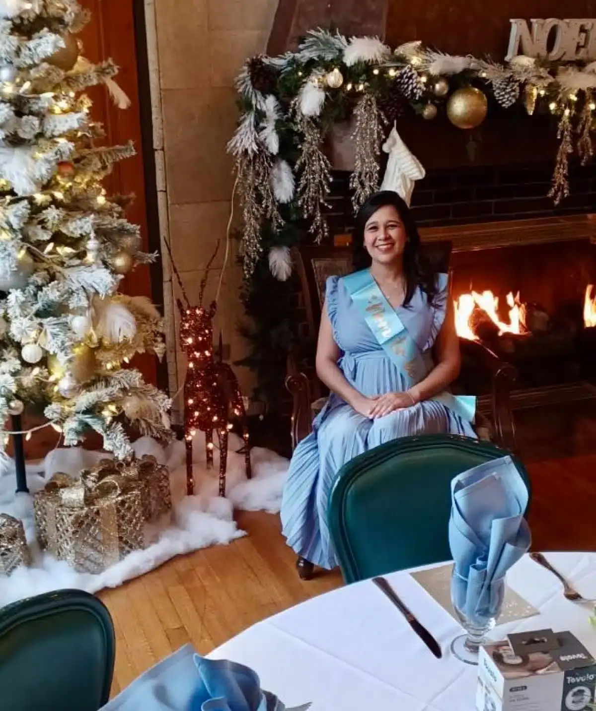 Elegant woman in blue dress sitting by a decorated fireplace at Cascades Manor.