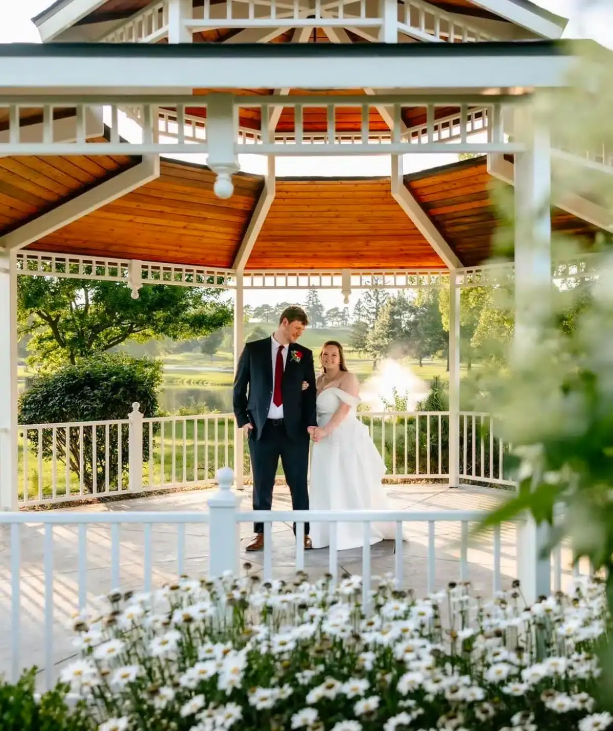 Wedding couple standing in gazebo at Cascades Manor, surrounded by lush greenery and flowers.