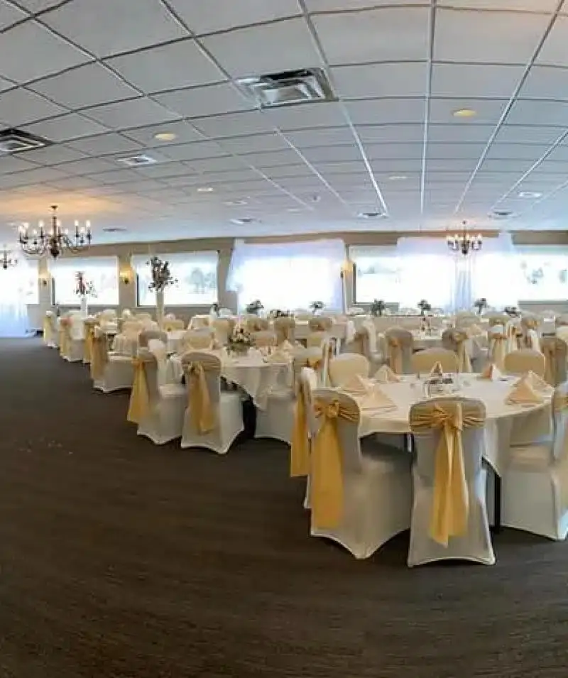 Banquet hall at Cascades Manor with round tables, white chair covers, and gold sashes for events.