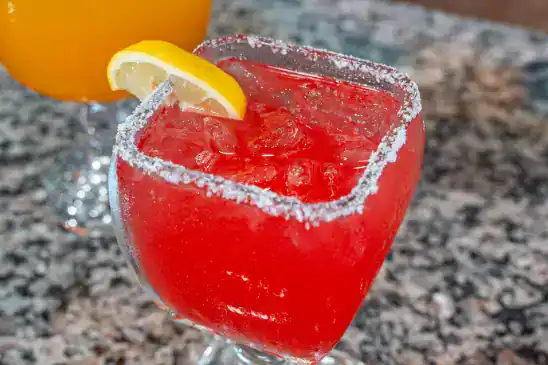 Red cocktail with lemon wedge in a glass on a granite countertop.