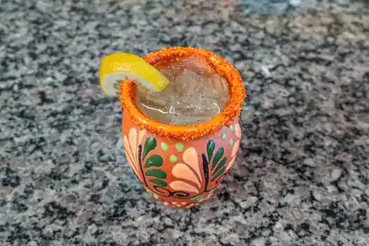 Colorful Mexican cocktail with lemon wedge on a granite countertop.
