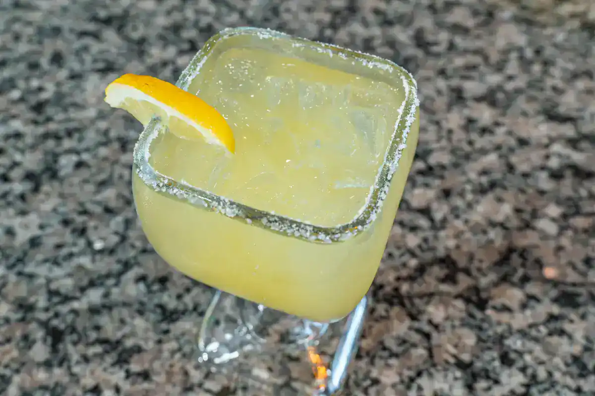 Lemon margarita with salted rim and lemon wedge on a granite table.
