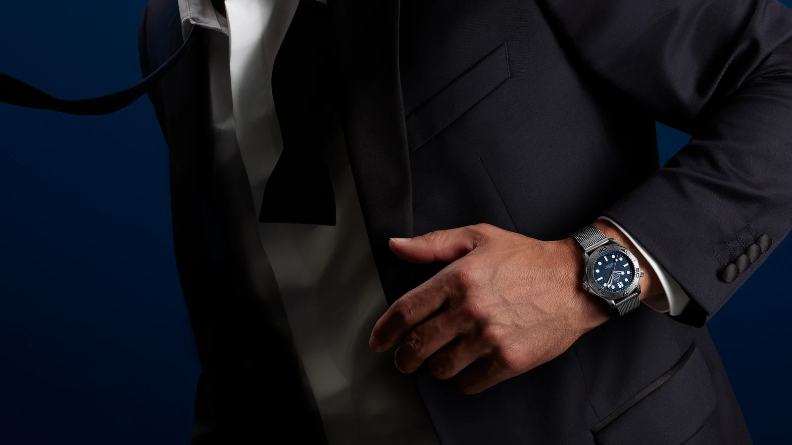 The James Bond edition from the Omega Seamaster James Bond Spectre collection worn on the wrist with a dark suit and white shirt, showing its titanium bezel, blue dial and steel mesh bracelet