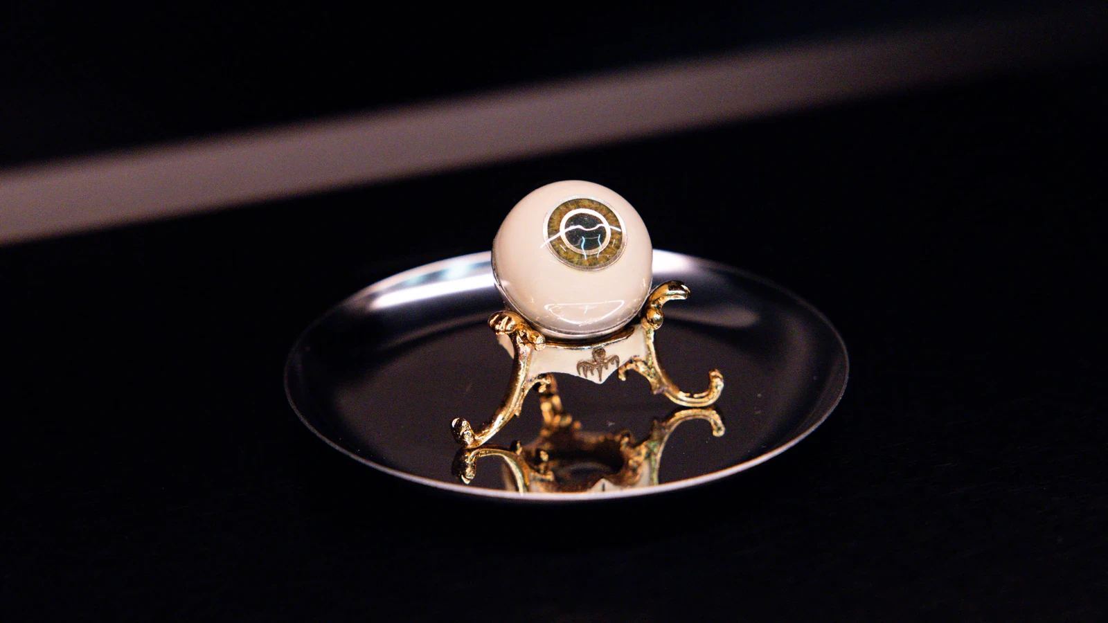 Bionic eye prop from No Time to Die on a gold stand bearing the Spectre octopus, displayed on a silver tray at OMEGA Glendale's Timeless Adversaries exhibition for the Omega Seamaster James Bond Spectre collection
