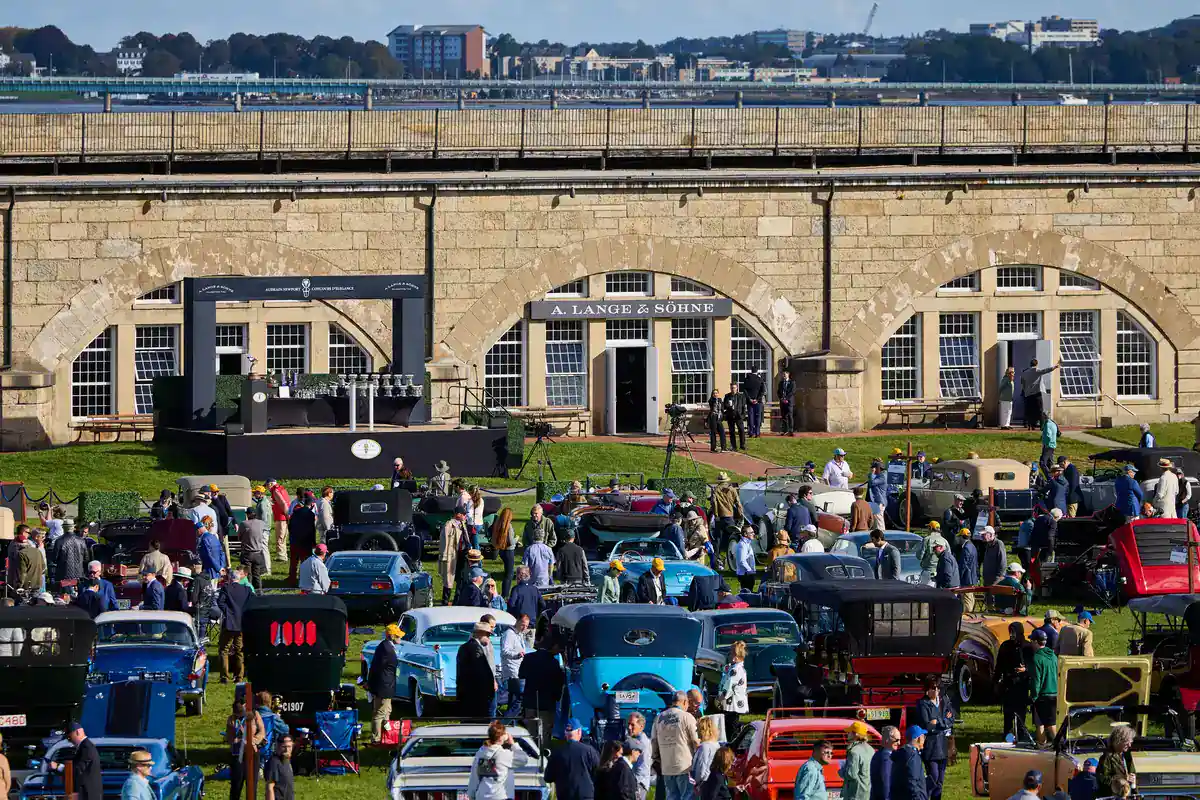 Audrain Newport Concours d'Elegance 2026 awards stage with trophies beside an A. Lange & Söhne arch in the stone walls of Fort Adams, with classic cars on the lawn