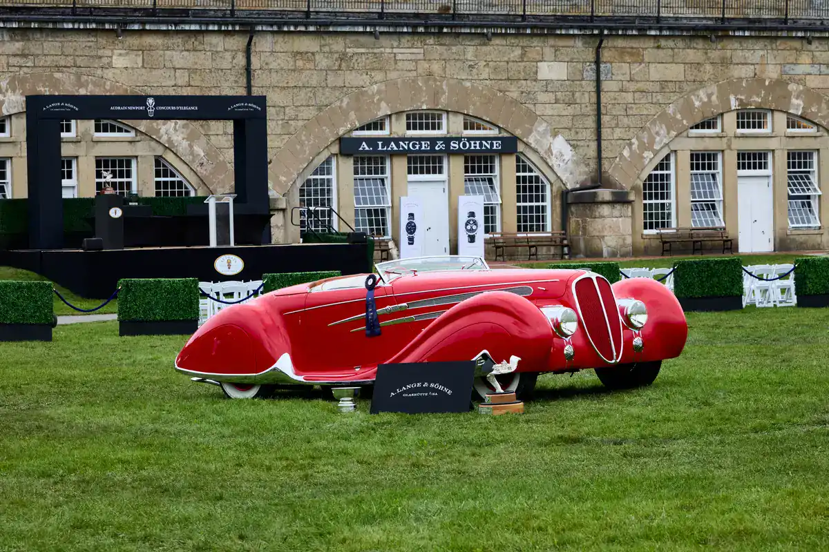 Red 1938 Delahaye 165 Figoni et Falaschi Cabriolet, Best of Show at the Audrain Newport Concours d'Elegance 2026, with its ribbon and trophy in front of an A. Lange & Söhne casemate