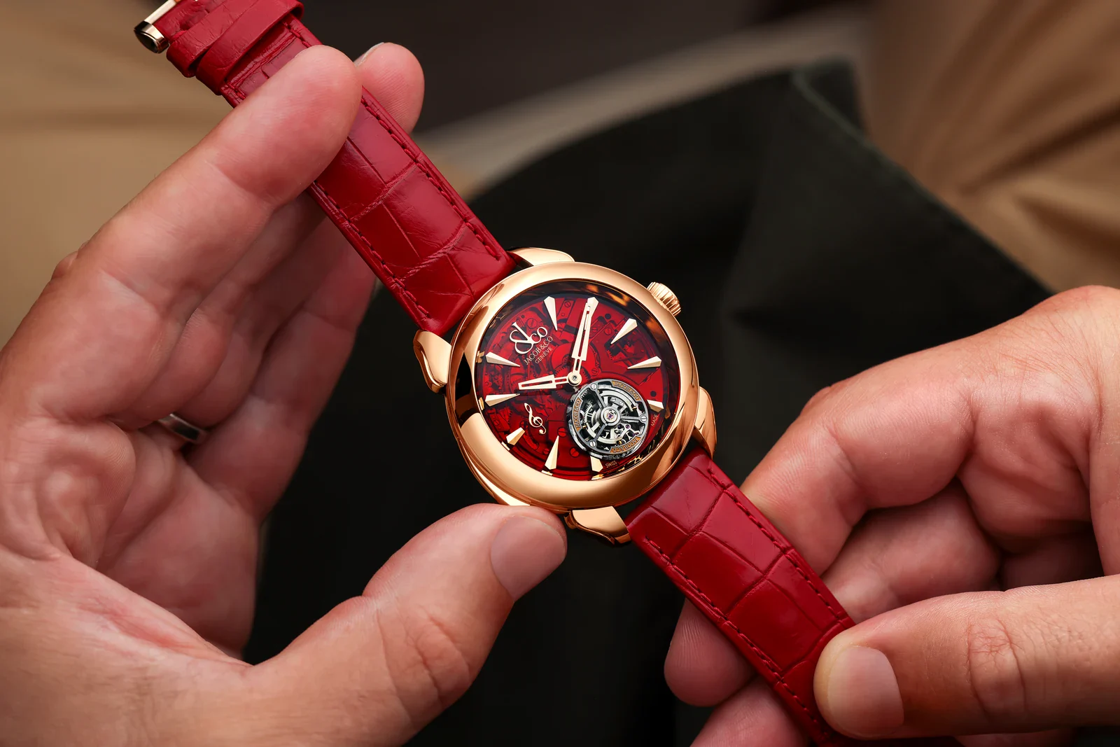 Hands holding the Jacob & Co. Palatial Flying Tourbillon Minute Repeater in 18K rose gold on its red alligator strap