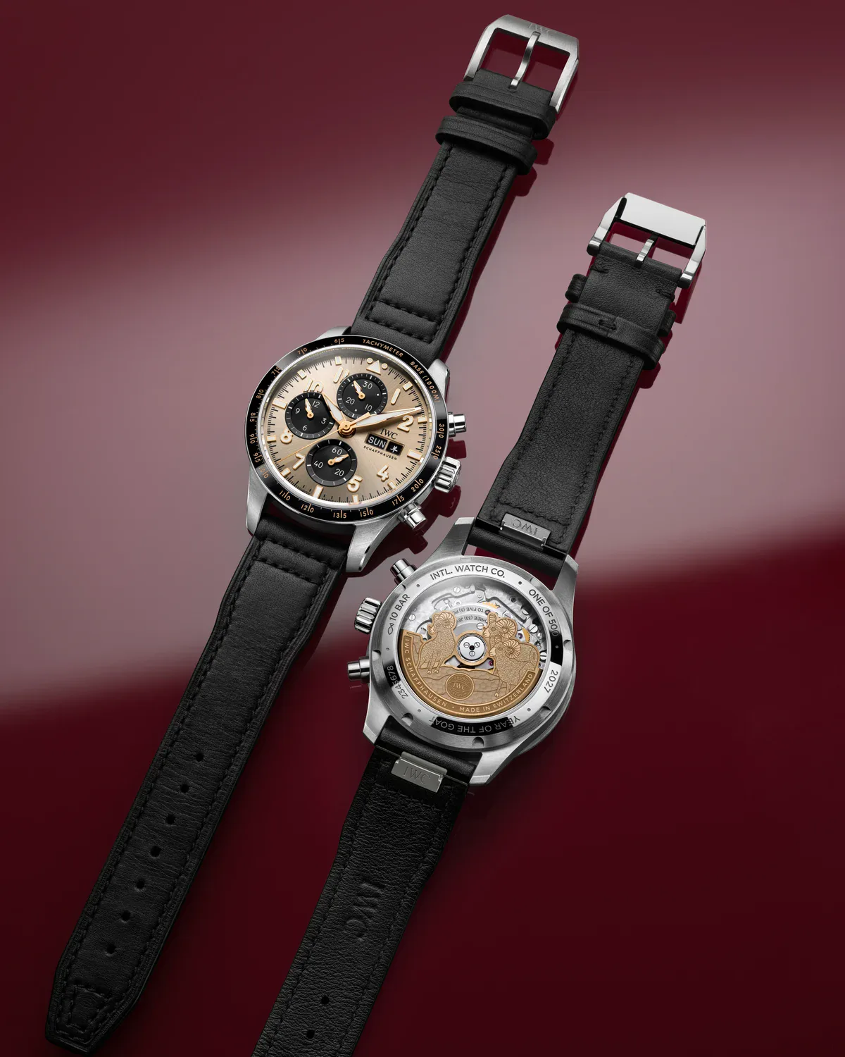 Front and caseback of the IWC Year of the Goat chronograph on black calfskin straps against a burgundy backdrop