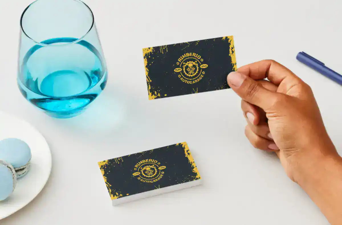 Person holding a black and yellow business card with a glass of water nearby.