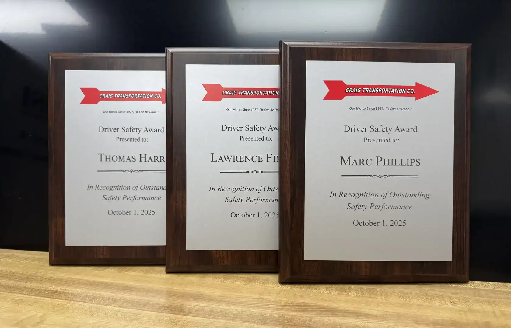 Three framed driver safety awards on a wooden surface.