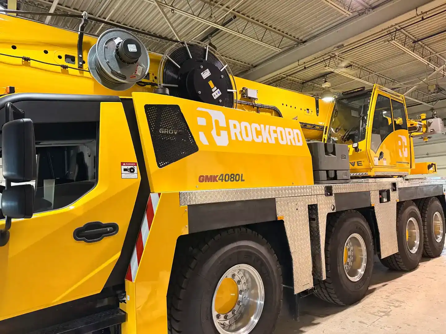 Yellow crane truck with Rockford Handicap Sign Inc. logo inside a warehouse.